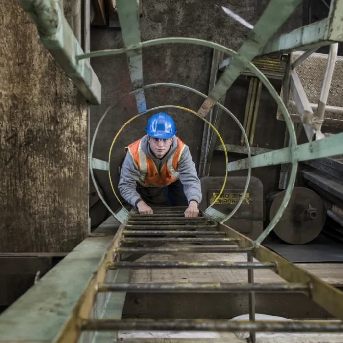 A male engineer climbing an inspection ladder outside in an industrial landscape